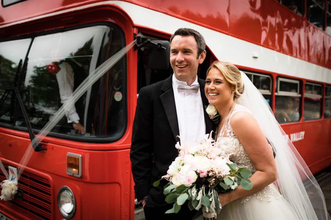 Bride and groom in front of red double decker bus 