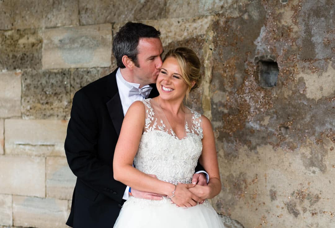 Groom kissing bride by old sea wall