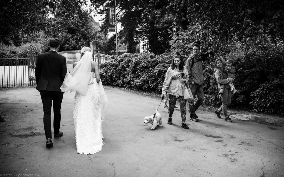 Bride and groom walking through park with members of public watching