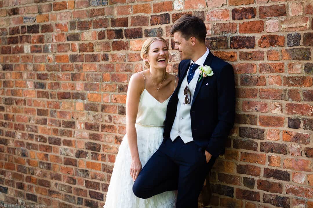 Bride and groom laughing against red brick wall at No 38 wedding Cheltenham