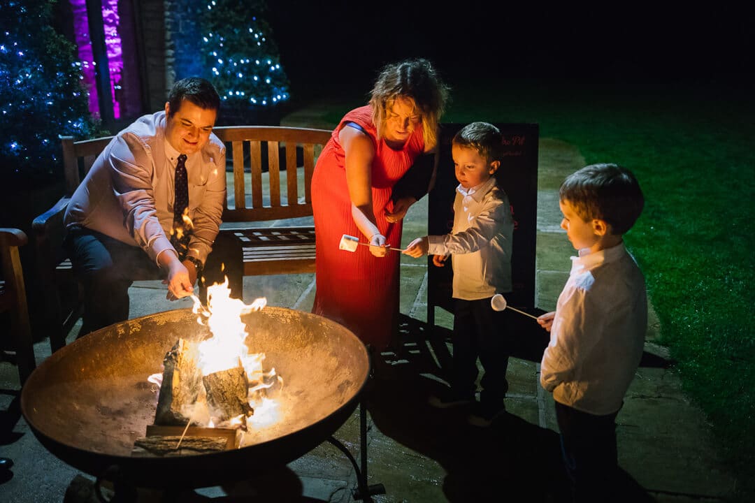 Guests toast marsh mellows over a fire at Kingscote Barn Wedding