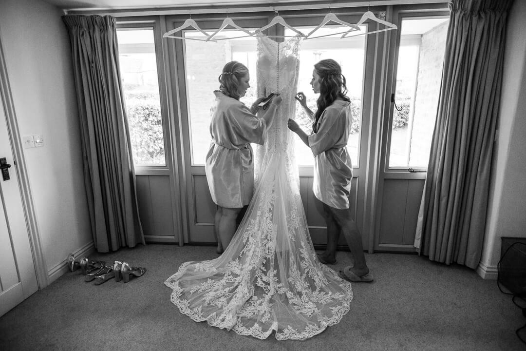 Natural wedding photo of bridesmaids getting wedding dress ready