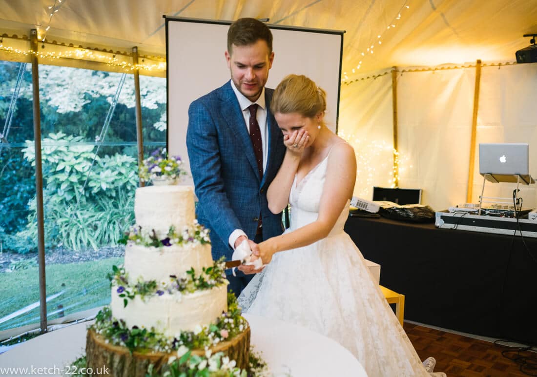 Bride and groom cutting large white wedding cake