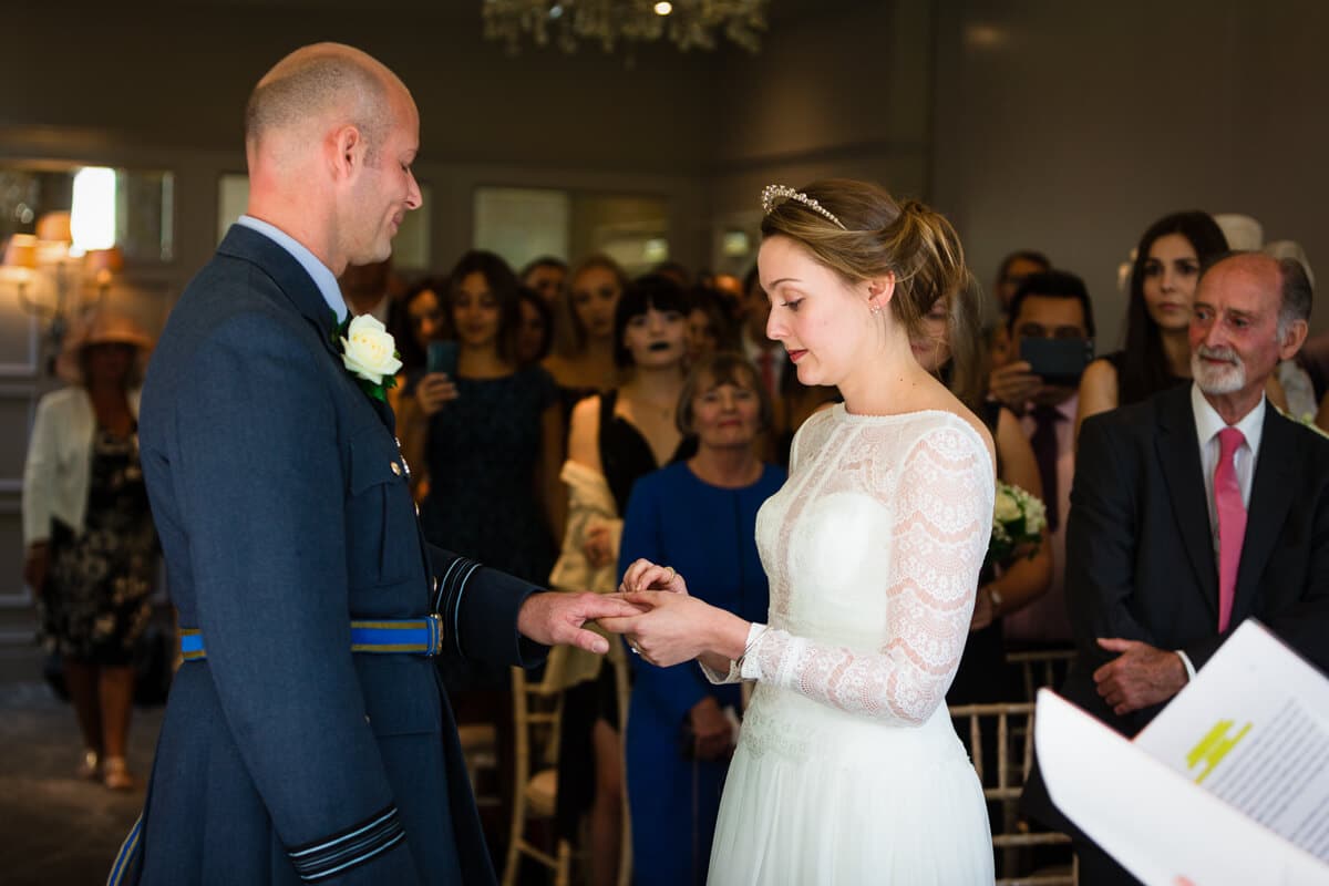 Bride putting ring on grooms finger at De Vere Latimer Estate wedding ceremony