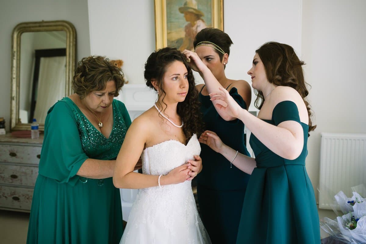 Bridesmaids and mum making a fuss over bride putting on wedding dress